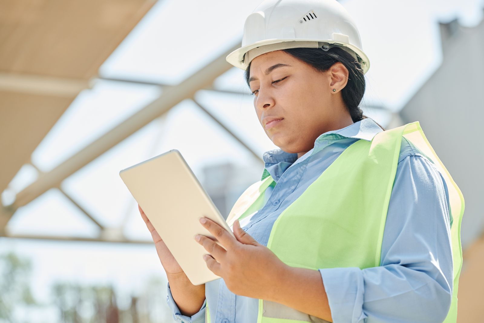 An engineer in a hard hat and high-visibility vest checking a tablet on site.